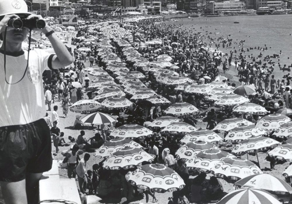 파라솔 꽃이 만개한 해운대해수욕장에서 망루 위 바다경찰서 수상요원이 망원경으로 주변을 살피고 있다. | 1988년 8월 | 부산일보